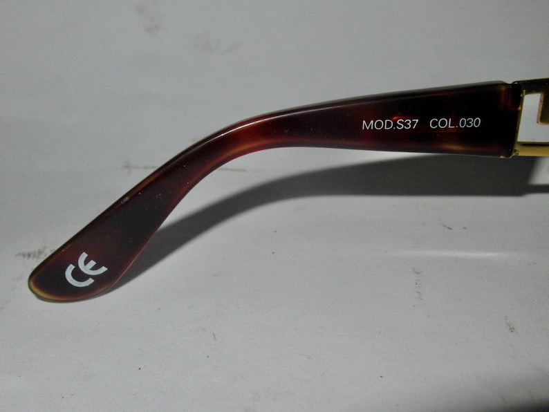 May include: Close-up of the brown tortoiseshell temple arm of a pair of eyeglasses. The arm is marked with the text "MOD.S37 COL.030" and the CE mark.