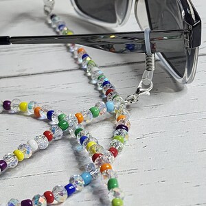 May include: A rainbow beaded eyeglass chain with clear crystal beads. The chain is attached to a pair of sunglasses with black frames.