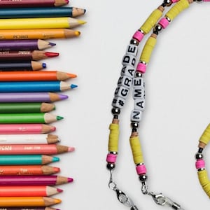 May include: A pair of yellow and pink beaded eyeglass chains with the words "#GRADE" and "NAME" spelled out in black letters on white beads.
