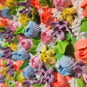 May include: A textured painting featuring a dense arrangement of three-dimensional floral shapes in vibrant shades of pink, orange, yellow, light blue, and purple, accented with small white blossoms and green leaves on a bright green background.