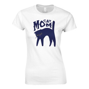 May include: White t-shirt featuring a navy blue cat illustration with the words "Cat Mom" in a stylized font. The cat has yellow eyes and a pink nose. The shirt is a casual, everyday wear item.