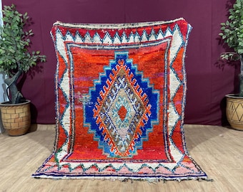 May include: A colorful Moroccan rug with a geometric pattern in shades of red, blue, white, and pink. The rug has a fringed edge and is made of wool.