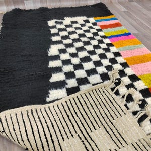 May include: A black and white checkered rug with a colorful striped border. The rug has a fringe border and is made of wool.