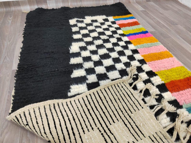 May include: A black and white checkered rug with a colorful striped border. The rug has a fringe border and is made of wool.