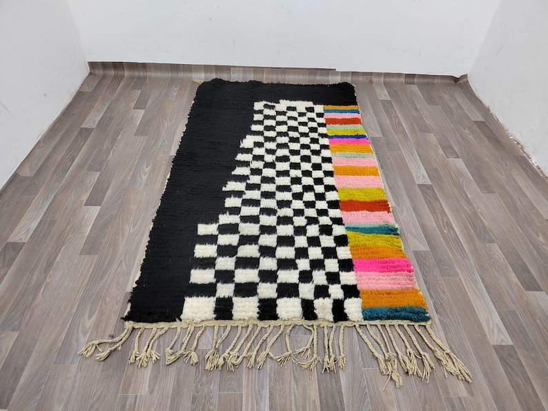 May include: A black and white checkered rug with a colorful stripe down the side. The rug has a fringe border.