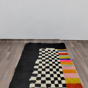 May include: A black and white checkered rug with a colorful stripe down the side. The rug is on a wood floor.