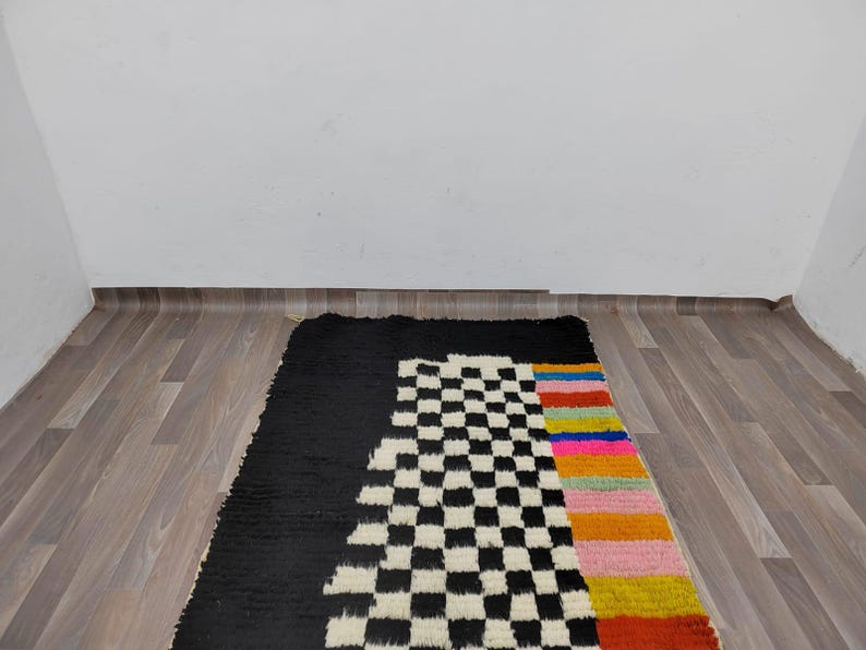 May include: A black and white checkered rug with a colorful stripe down the side. The rug is on a wood floor.