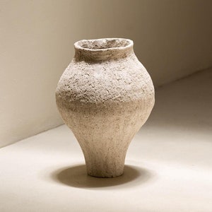 May include: A white ceramic vase with a textured surface. The vase has a rounded body and a narrow neck.