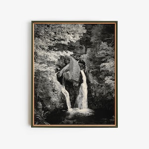 Puede incluir: Una fotografía en blanco y negro de una cascada que cae por un acantilado rocoso, rodeada de exuberante vegetación.