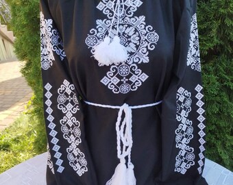 May include: A black embroidered blouse with white geometric patterns and white tassels. The blouse has a round neckline and long sleeves.