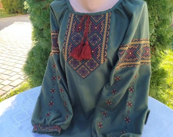 May include: A green embroidered blouse with a red tassel. The embroidery features geometric patterns in shades of gold, red, and brown.