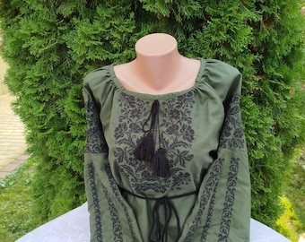 May include: A green embroidered blouse with black floral embroidery and black tassels. The blouse has a round neckline and long sleeves.