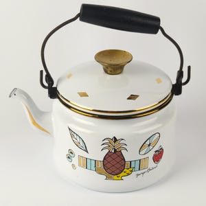 May include: White enamelware kettle with a black handle and spout. The kettle features a colourful design of a pineapple, leaves, and fruit. The lid has a gold-coloured knob and gold diamond accents. The handle is made of black wood.