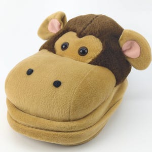 Puede incluir: Zapatilla de felpa con forma de mono en tonos marrón y beige. La zapatilla presenta una cara de mono con ojos grandes, orejas con detalles rosas y un cierre de cremallera. Diseño de cabeza de mono.