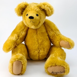 Può includere: Un orsacchiotto giallo dorato con una morbida pelliccia strutturata. L'orso ha un naso nero e piccoli occhi scuri. Le sue zampe sono di un colore marrone chiaro. L'orso è seduto in posizione eretta con le braccia e le gambe distese.