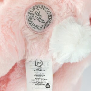 May include: Close-up of a pink plush toy with a white pom-pom and a Disney Store label. The label features the Disney Store logo and text. The plush toy has a soft, fluffy texture.