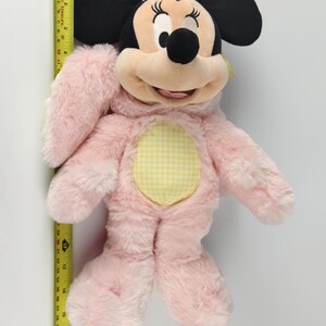 May include: A plush Minnie Mouse doll, primarily pink with black ears and a yellow gingham belly. The doll is approximately 17 inches tall, with a smiling face and detailed facial features.