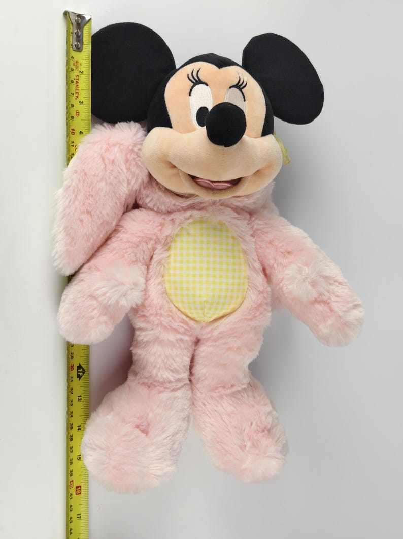 May include: A plush Minnie Mouse doll, primarily pink with black ears and a yellow gingham belly. The doll is approximately 17 inches tall, with a smiling face and detailed facial features.