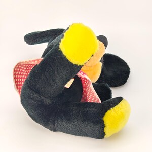 May include: A plush toy dog with black fur, yellow paws, and a peach-colored face. The dog is wearing a red polka-dot dress. The toy is lying on its side against a white background.