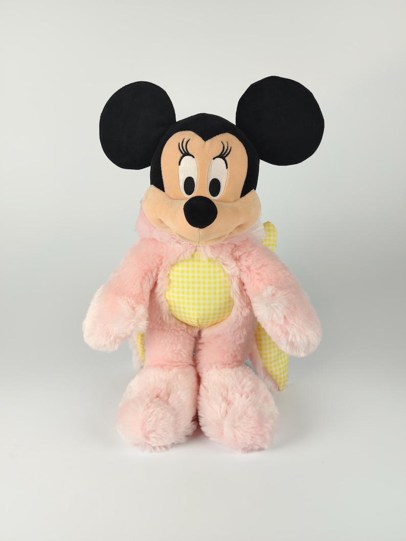 May include: A plush Minnie Mouse doll wearing a pink and yellow butterfly costume. The doll has black ears, a black nose, and a pink and yellow gingham pattern on the chest. The doll is approximately 12 inches tall.