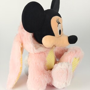 May include: A plush Minnie Mouse dressed as a bunny. The toy features a black head with large ears, a pink bunny suit with yellow gingham accents, and a white fluffy tail. The plush is soft and cuddly.
