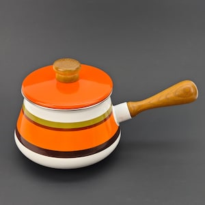 May include: A vintage orange and white enamel saucepan with a wooden handle and lid. The saucepan features horizontal stripes in orange, white, brown, and olive green. The lid has a wooden knob.