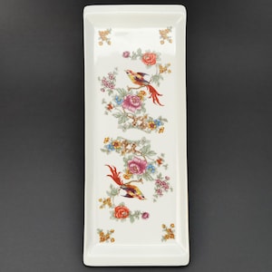 Puede incluir: Bandeja rectangular de cerámica blanca con diseño floral y de pájaros. La bandeja presenta un colorido patrón de flores y pájaros en tonos rojos, rosas, amarillos y azules. La bandeja es rectangular con esquinas redondeadas.