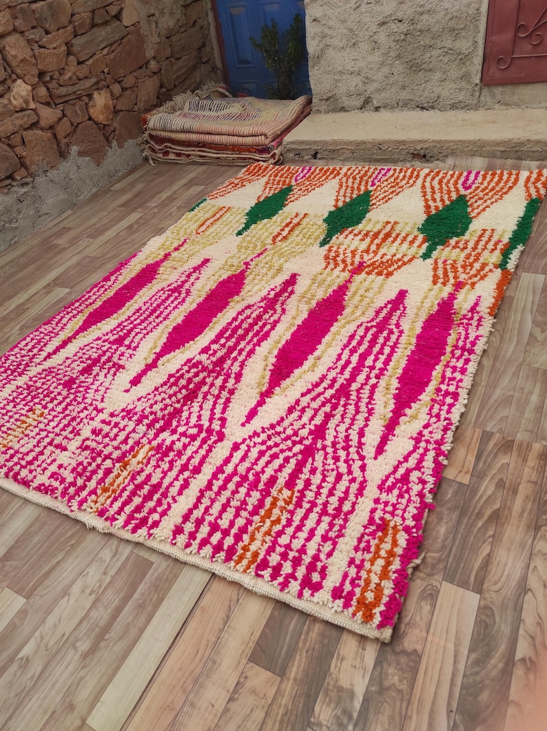 Puede incluir: Una alfombra rectangular con un dise&ntilde;o vibrante. La alfombra presenta un fondo crema con un patr&oacute;n de formas rosas, naranjas y verdes. La alfombra est&aacute; colocada sobre un suelo de madera, mostrando su textura y colores.