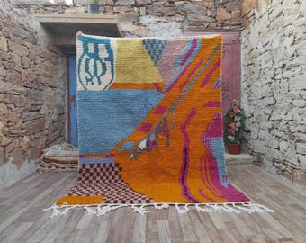 May include: A colorful Moroccan rug with geometric patterns in shades of blue, orange, pink, and yellow. The rug has a fringe border and is made of wool.