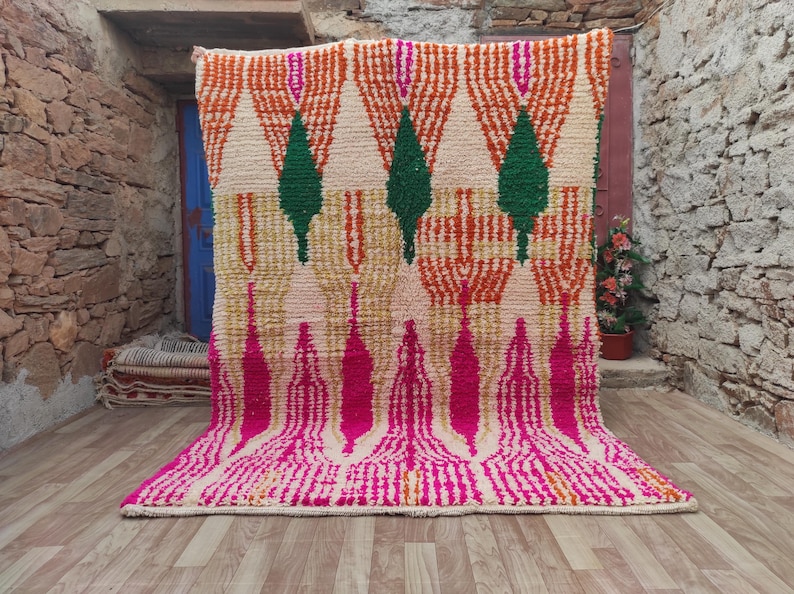 Puede incluir: Una alfombra grande y colorida con un patr&oacute;n geom&eacute;trico. La alfombra presenta un fondo crema con dise&ntilde;os en naranja, verde y rosa. La alfombra se exhibe en un entorno al aire libre, agregando un toque de calidez y estilo al espacio.
