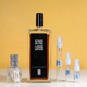 May include: A set of four perfume bottles, including a large bottle of Serge Lutens Le Participe Passé perfume. The bottles are clear glass with black and silver accents. The large bottle is 12 ml and the smaller bottles are 3 ml, 5 ml, and 10 ml.