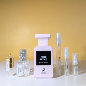 May include: A set of perfume bottles in various sizes, including a larger bottle with a pink label that reads "ROSE PETALS EAU DE PARFUM" and a deer logo. The smaller bottles are clear glass with black labels indicating the volume in milliliters.