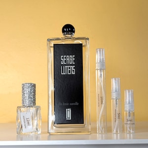 May include: A set of four glass perfume bottles with spray tops. The largest bottle is a clear glass bottle with a black label that reads "Serge Lutens Un Bois Vanille". The other three bottles are smaller and have labels indicating their volume: 12 ml, 10 ml, 5 ml, and 3 ml.