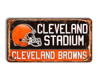 May include: A rectangular metal sign with a distressed finish featuring an orange football helmet graphic, the text CLEVELAND STADIUM in white, and the text CLEVELAND BROWNS in white on an orange background at the bottom of the sign.