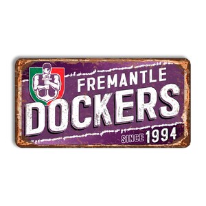 May include: A rectangular, distressed metal sign featuring the text "FREMANTLE DOCKERS" in white, bold letters on a purple background. The sign includes a logo with a figure holding an anchor and the text "SINCE 1994". The edges are rusty.