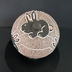 Può includere: Tazza in ceramica bianca con manico nero e la scritta "But First, Coffee" in nero. La tazza è posta su uno sfondo sfocato, suggerendo un ambiente accogliente.