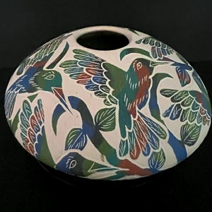 May include: A white ceramic vase with a round shape and a large opening at the top. The vase is decorated with colourful hummingbirds and foliage in shades of blue, green, and red. The design is hand-painted.