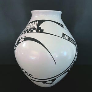 May include: White ceramic vase with black geometric patterns. The vase has a rounded body and a narrow neck. The black designs include lines, shapes, and floral motifs, creating a striking contrast against the white background. The vase is a decorative item.