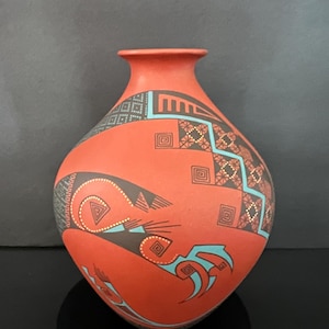 May include: A terracotta-colored ceramic vase with intricate geometric designs in black, turquoise, and brown. The vase features a rounded body and a narrow neck, showcasing a Southwestern or Native American aesthetic.