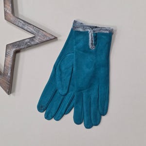 May include: Teal gloves with faux fur trim and button detail. The gloves are made of a soft material, suitable for cold weather. A wooden star is in the background.