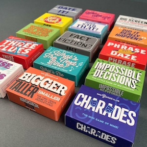 Könnte beinhalten: Eine Sammlung farbenfroher Mini Games Club-Boxen. Die Boxen zeigen verschiedene Spieltitel wie "Charades", "Phrase Daze" und "Bigger or Smaller". Jede Box hat ein einzigartiges Farbschema und Textdesign, perfekt für Spieleabende.