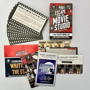May include: A board game called "Escape from the Movie Studio" with a red and black box and various cards. The cards feature movie-themed graphics and text, including "Now Shooting" and "A Midsummer Night's Dream". Includes instructions and puzzle cards.