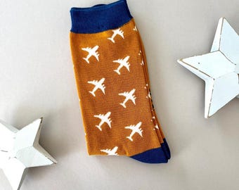 May include: A pair of socks with a mustard yellow background and white airplane designs. The socks have a navy blue cuff.