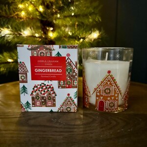 Op de afbeelding: Een witte doos met een gingerbreadhuispatroon en de tekst "Gisela Graham London Gingerbread Scented Candle". Een glazen kaars pot met een gingerbreadhuispatroon en een witte kaars erin.