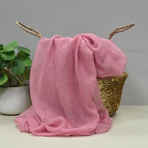 May include: A pink sheer scarf with a subtle sparkle, draped over a gold sequined basket.
