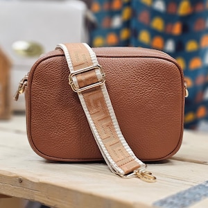 May include: A brown leather crossbody bag with a white and brown patterned strap. The bag has a gold clasp and a gold chain.