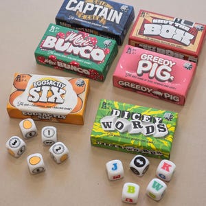 May include: A selection of board games in various boxes, including "Captain," "Mini Bunco," "EggSactly Six," "Shut the Box," "Greedy Pig," and "Dicey Words." Dice with numbers, symbols, and letters are also visible. The games are suitable for ages 8 and over.
