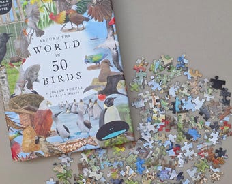 May include: A jigsaw puzzle box and scattered pieces. The box features a colorful illustration of various birds with the text "AROUND THE WORLD IN 50 BIRDS". The puzzle pieces are in various colors and shapes, suggesting a complex design.