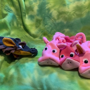 May include: Three pink pig hand puppets with black eyes and a brown and black dragon hand puppet.