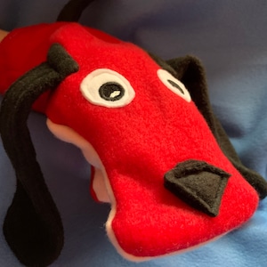 May include: Red felt hand puppet shaped like a dog with black felt ears, nose, and tail. The puppet has white felt eyes.